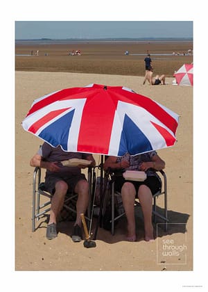 People relax under a Union Flag umbrella on a sandy beach, capturing a quintessential British seaside moment.