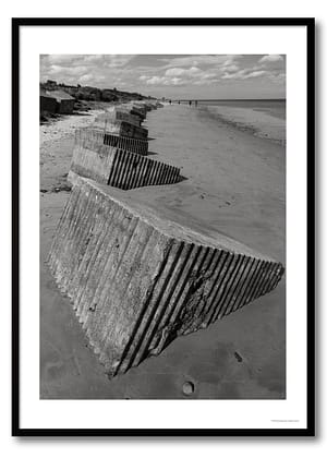 Coastal defences photography print showing a line of concrete anti-tank blocks on a beach in monochrome.
