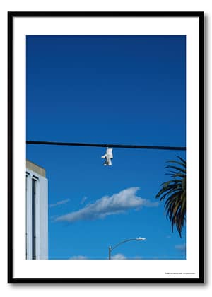 Los Angeles shoefiti photography print showing white boots hanging from a power line against a deep blue sky and palm tree.