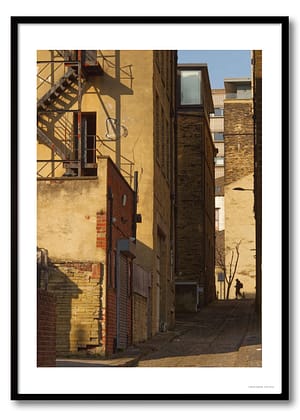 Backstreet urban photography print showing long geometric shadows across a narrow brick lane with a silhouetted figure.
