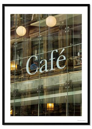 A 70x50cm architectural photography print titled 'Wiring Jolly Beard' featuring a modernist café exterior. Reflections of older urban buildings overlay a view of the interior's transitioning floor levels, industrial lighting, and a lone figure seated behind a large white letter 'C' from 'Cafe' signage.