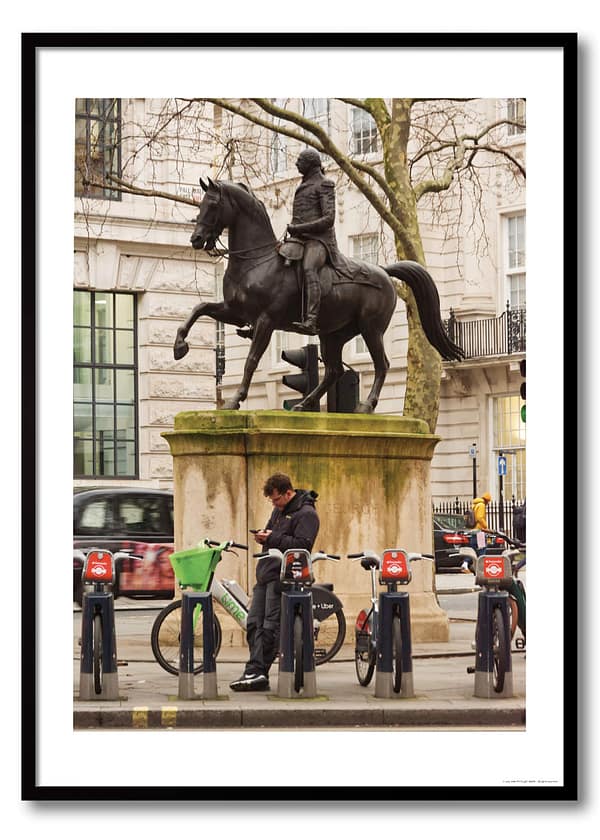 London street photography print showing man scrolling phone below King George equestrian statue, surrounded by Santander and Lime hire bikes on Pall Mall