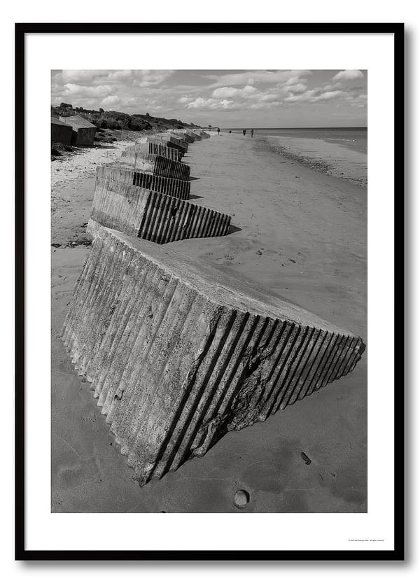 Coastal defences photography print showing a line of concrete anti-tank blocks on a beach in monochrome.