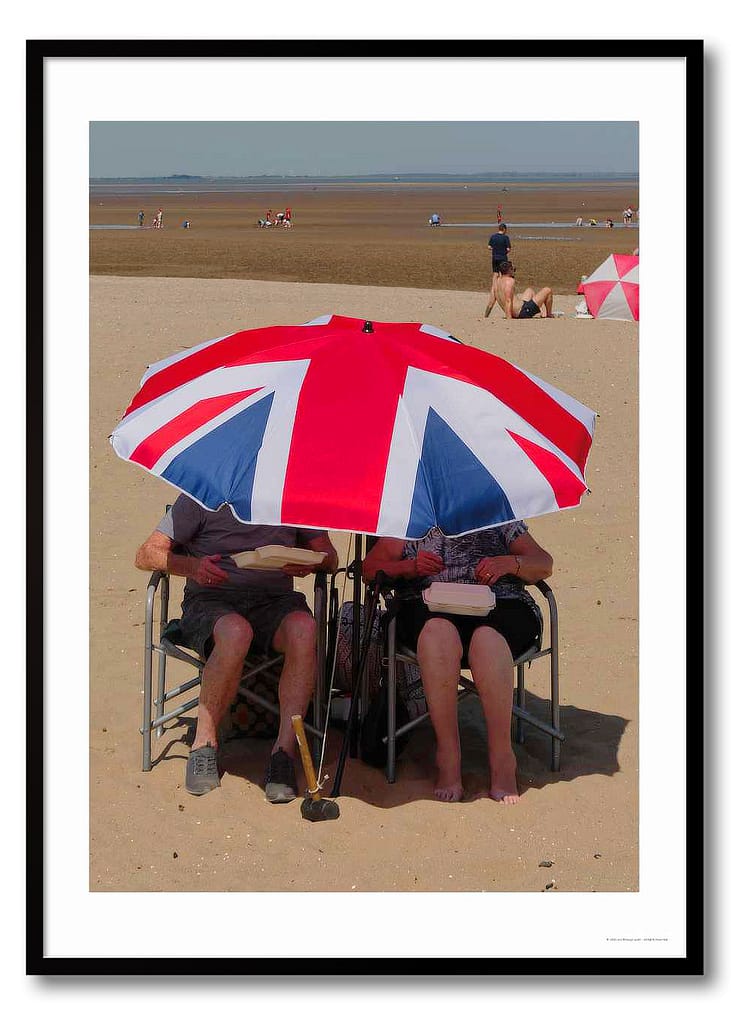Candid British summer photography print showing two people under a Union Jack umbrella eating fish and chips on Humber estuary beach
